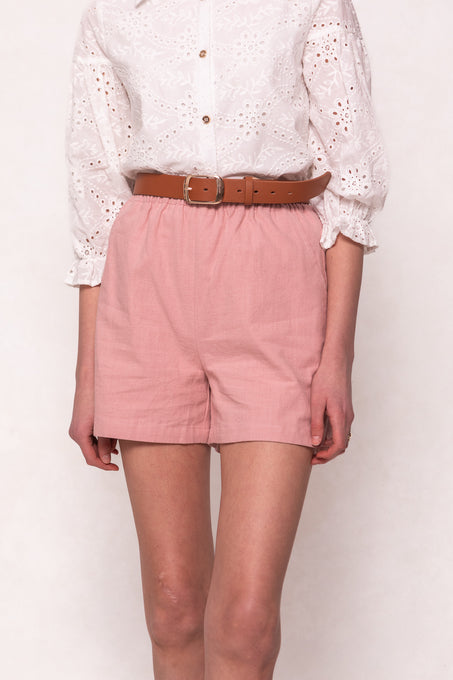 A person wears a white embroidered three-quarter sleeve blouse with Ivy City Co’s Skye Shorts in Pink, featuring a brown belt. The photo is cropped from shoulders to mid-thigh.