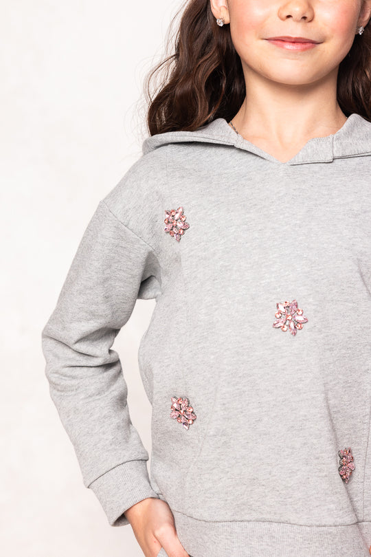 close up of a young girl in a grey hoodie with pink rhinestones against a white background