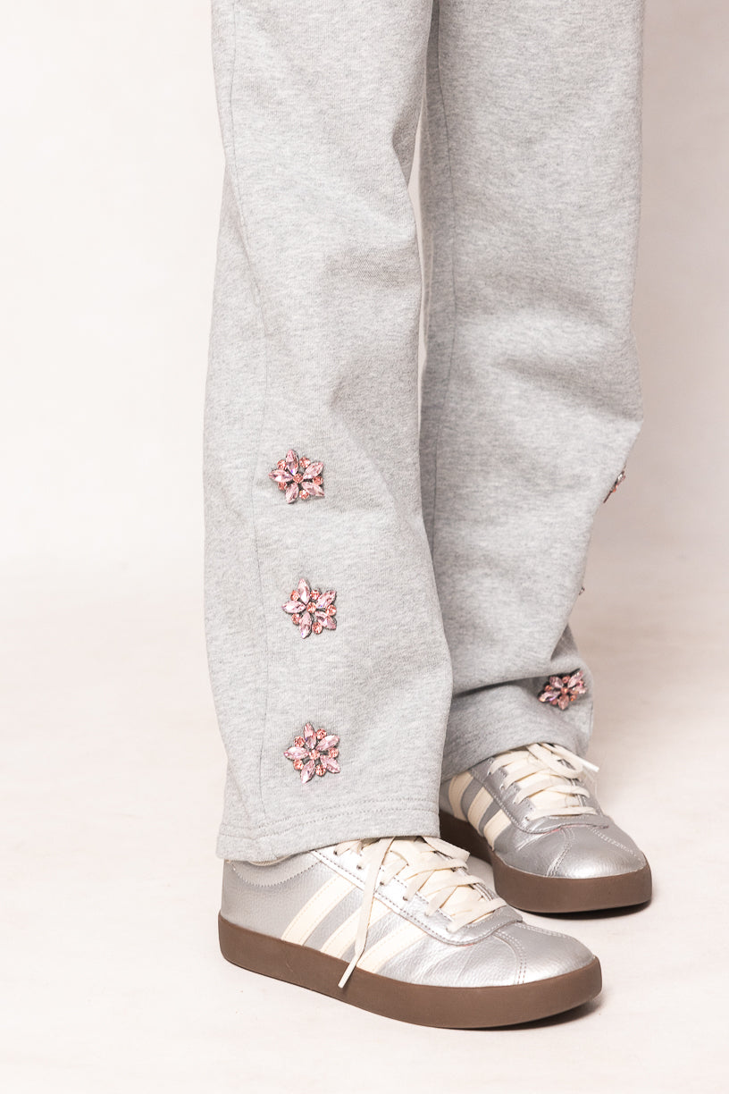 Grey sweatpants with pink jeweled flowers and silver sneakers against a white background