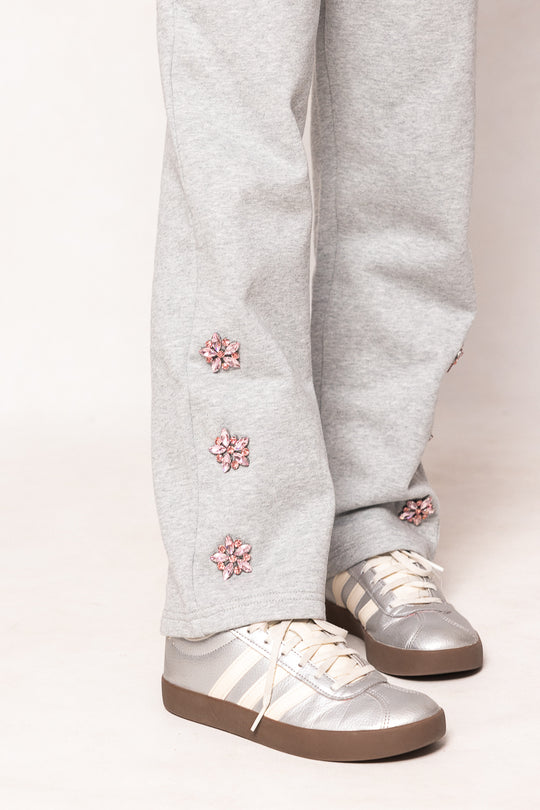 Grey sweatpants with pink jeweled flowers and silver sneakers against a white background