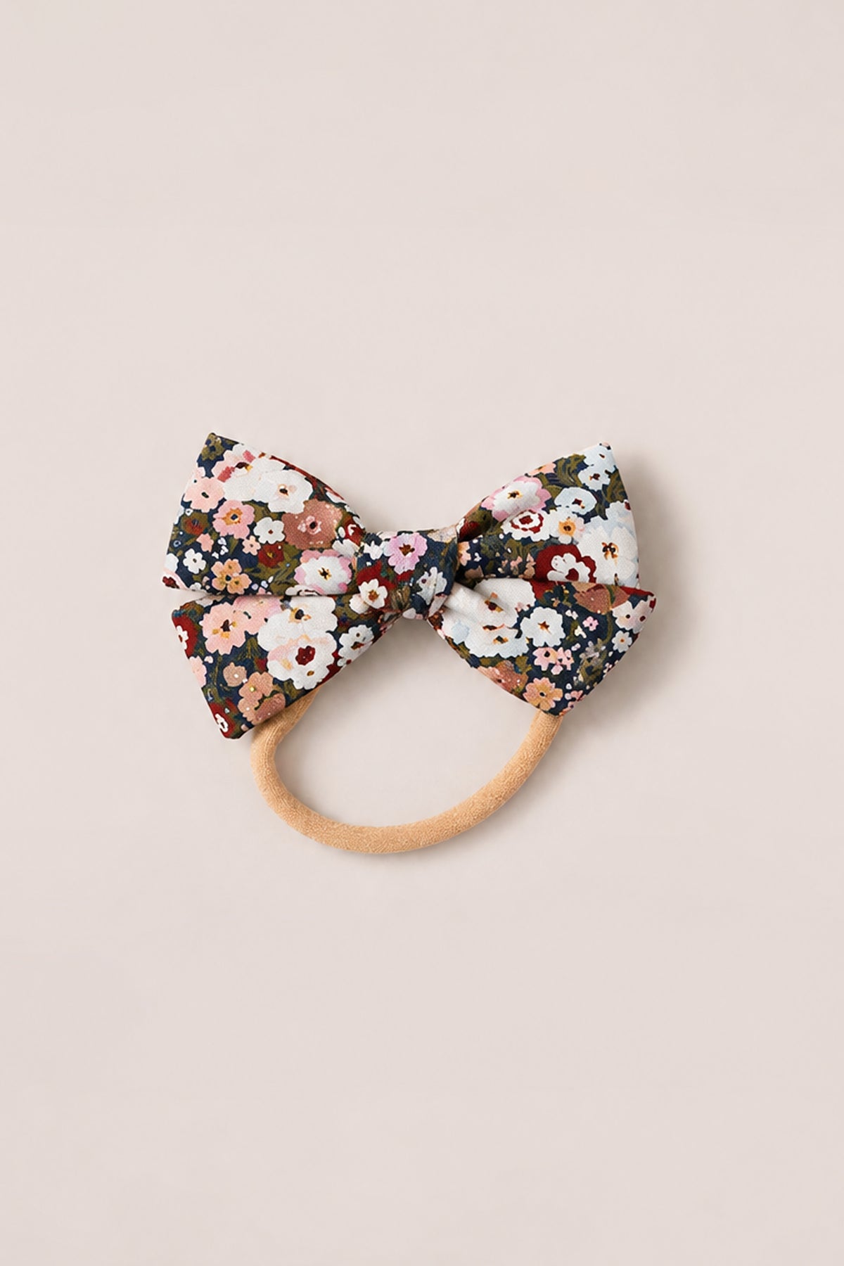 Introducing the Hair Bows in Midnight Garden by Ivy City Co—an elegant hair accessory featuring a large fabric bow adorned with a vibrant floral pattern in red, pink, white, and green. Reminiscent of Ivy City Co’s signature femininity, this charming hair tie is set on a beige elastic band and elevates any look with the enchanting spirit of Midnight Garden. Photographed delicately on a light background.