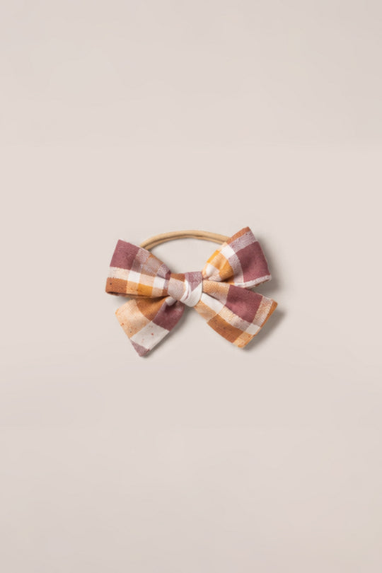 The Ivy City Co Hair Bows in Spiced Plaid feature soft cotton in pink, yellow, and white hues, attached to a tan elastic band and showcased against a light beige background.