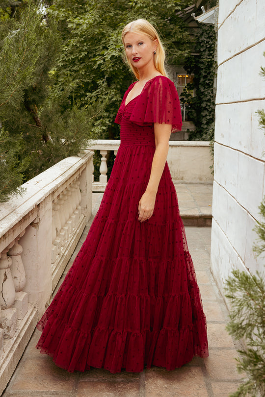 Woman in a red dress standing on a stone pathway with greenery in the background