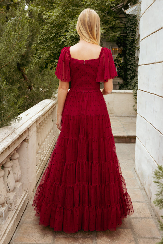 Woman in a red dress standing on a stone pathway with greenery in the background
