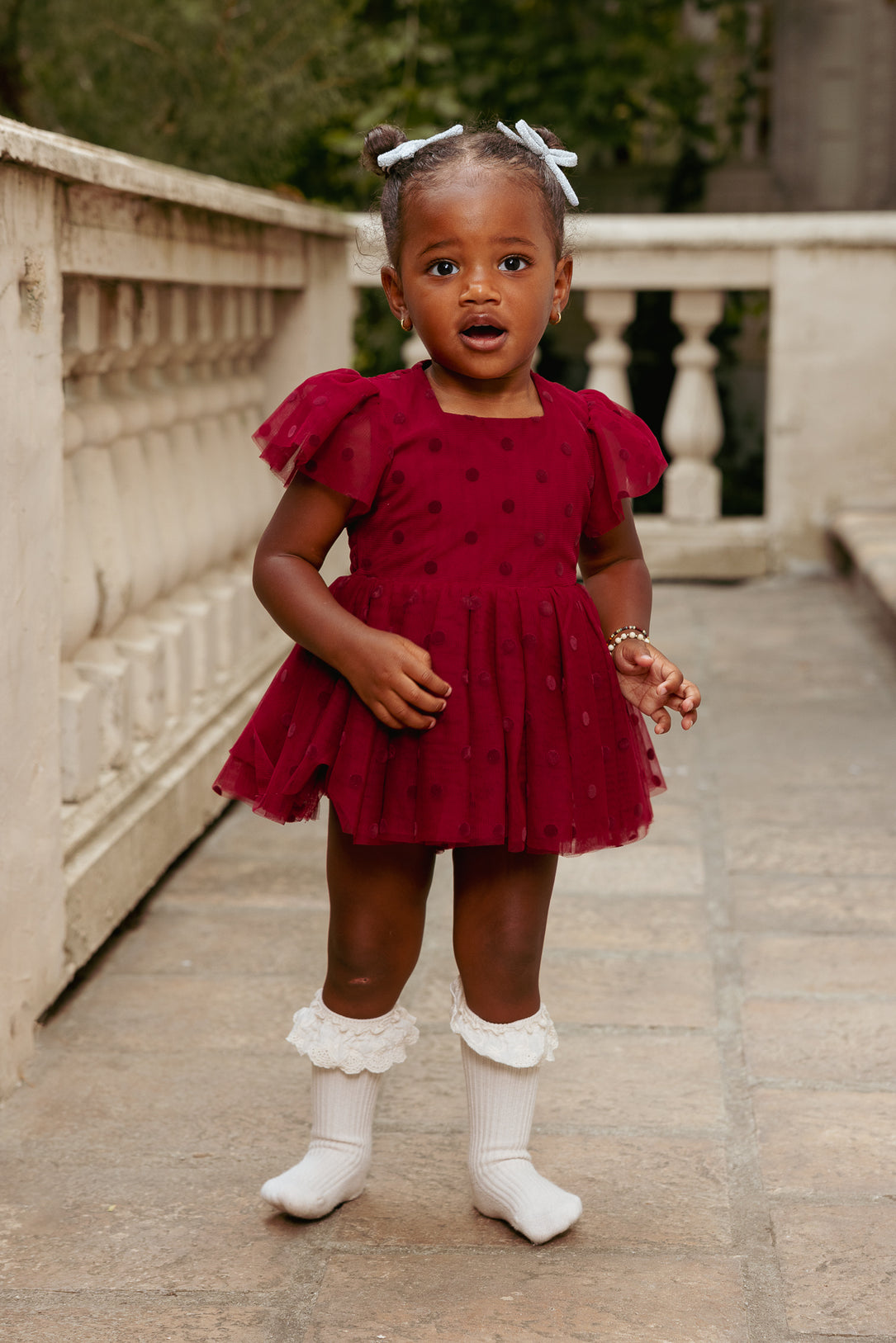 Young girl in a red dress with white socks standing on a stone path.