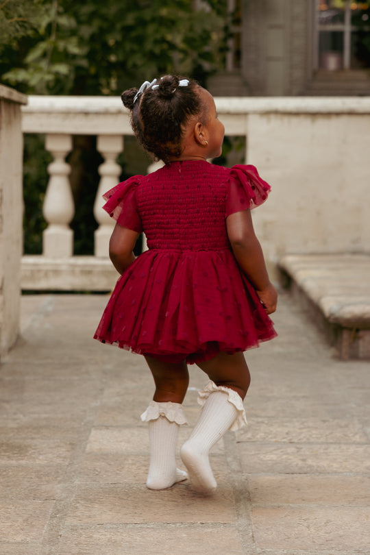 Child in a red dress walking outdoors on a stone path.