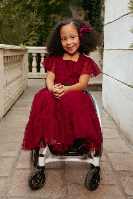 Young girl in a red dress sitting in a wheelchair on a stone pathway.