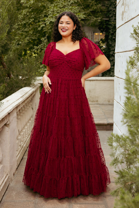 Woman in a burgundy evening gown standing outdoors on a stone path.