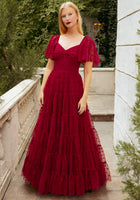 Woman in a red dress standing outdoors with greenery in the background
