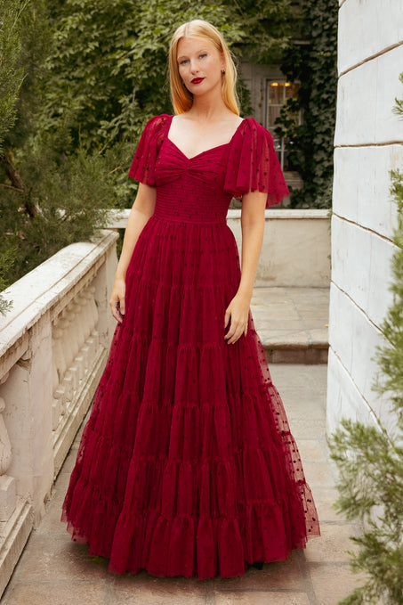 Woman in a red dress standing outdoors with greenery in the background
