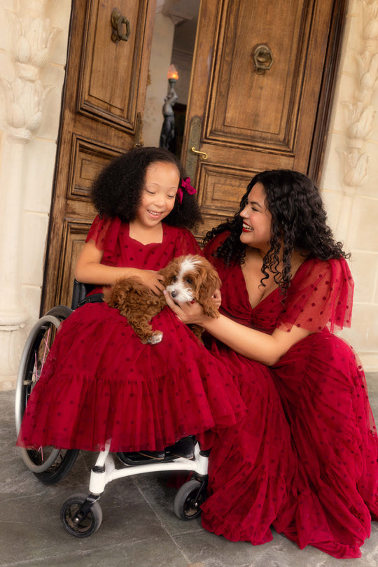 Two women in red dresses with a dog in front of a wooden door.