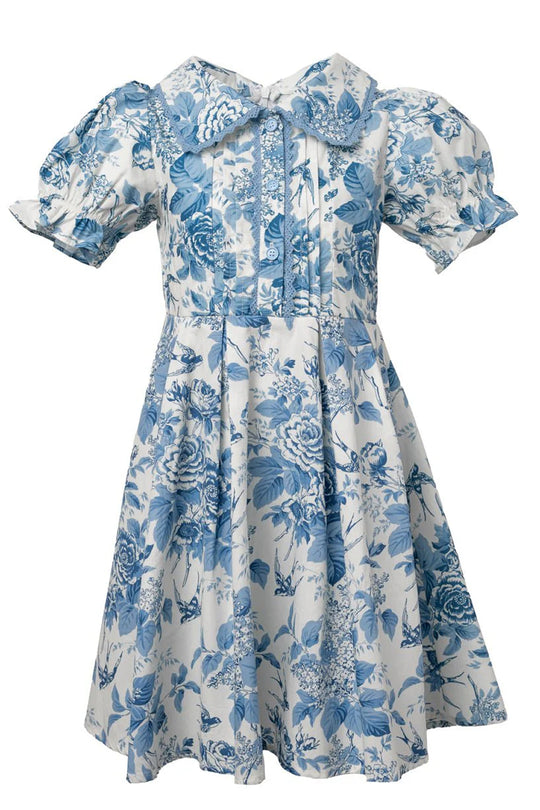 The Ivy City Co Mini Sophia Dress in Blue Floral is a charming girls’ spring dress with short puffed sleeves, a large bow-collar, pleated bodice, and knee-length skirt.
