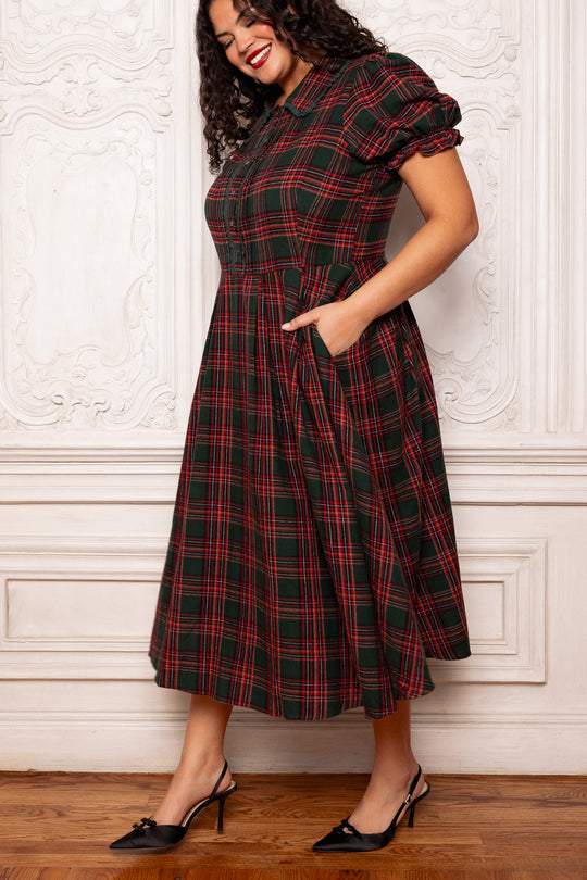 Woman wearing a red and green plaid dress against a white wall.