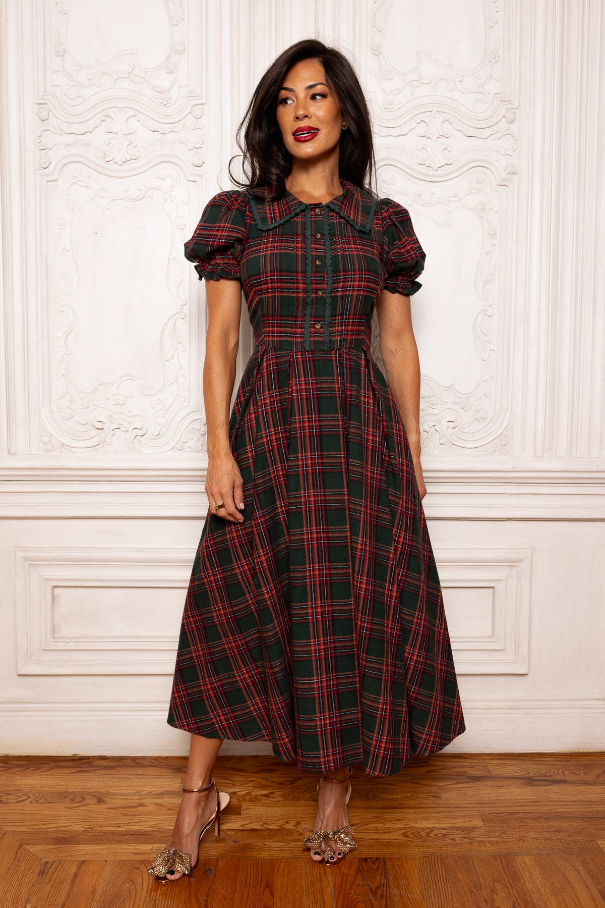Woman wearing a red and green plaid dress against a white wall.