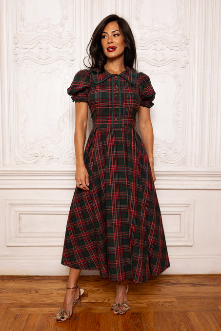 Woman wearing a red and green plaid dress against a white wall.