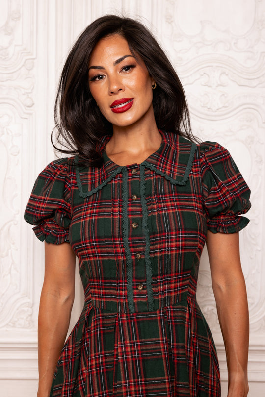 Woman wearing a red and green plaid dress against a white wall.