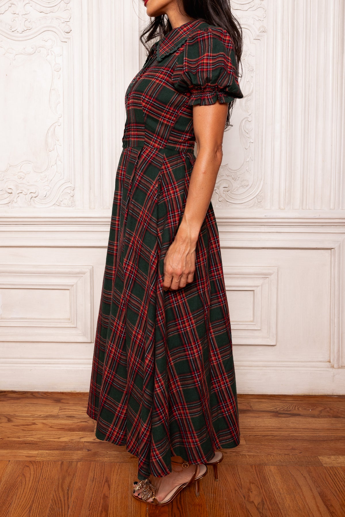 Woman wearing a red and green plaid dress against a white wall.