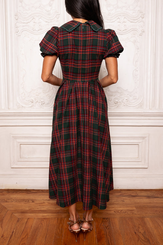 Woman wearing a red and black plaid dress against a white wall.
