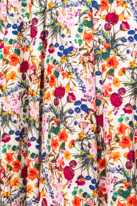 The Sophia Dress in Multicolor Floral by Ivy City Co features a dense pattern of red, pink, orange, yellow, blue, and purple flowers on soft off-white fabric with textured folds—ideal for a charming statement look.