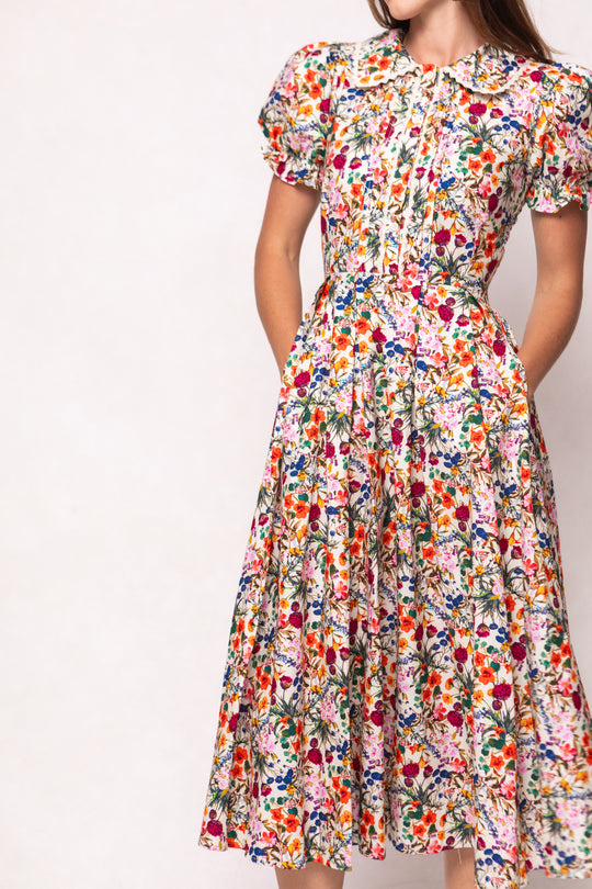 A woman models the Ivy City Co Sophia Dress in Multicolor Floral, a vintage-inspired cotton midi with a Peter Pan collar and pockets, posing against a plain background.