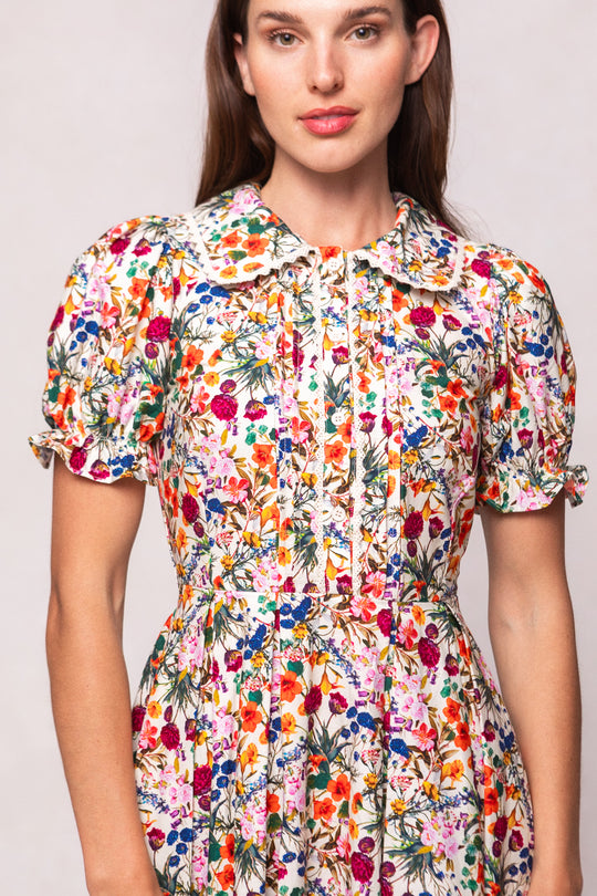 A woman wears the Ivy City Co Sophia Dress in Multicolor Floral, a short-sleeved cotton midi dress with ruffled sleeve edges, pleated details, and a fitted waist. She stands facing forward against a neutral background.