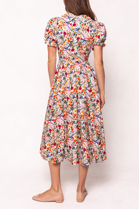 A woman faces away wearing the Ivy City Co Sophia Dress in Multicolor Floral—a cotton midi with a fitted waist, flared skirt, collar, and colorful floral print—paired with nude flats.