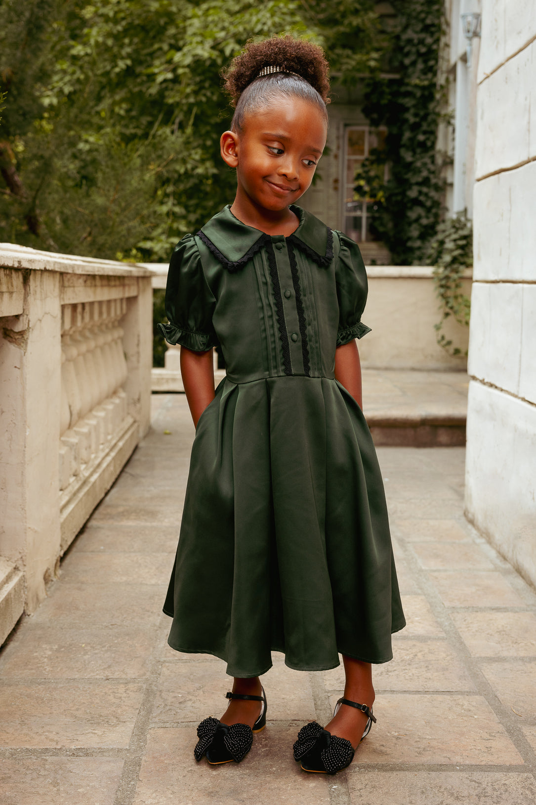 Young girl in a green dress standing outdoors on a stone path.