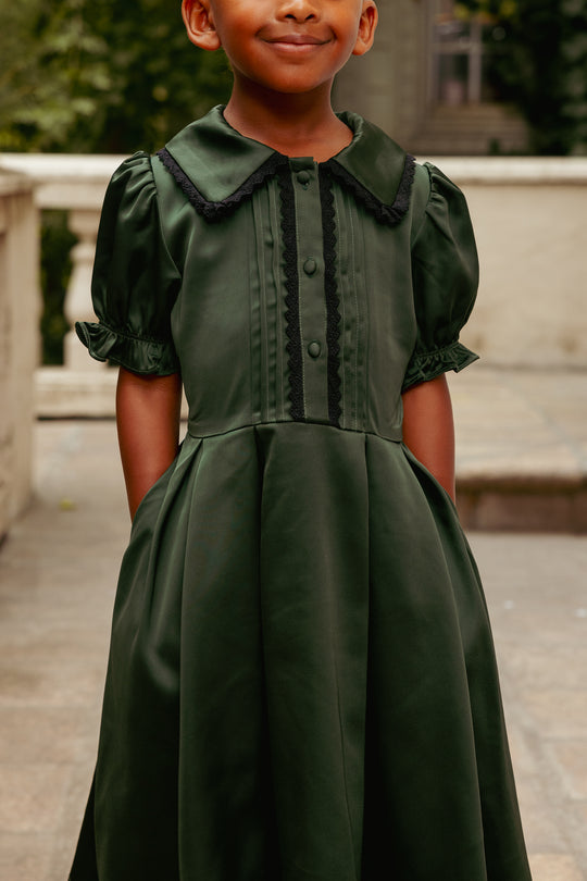 Child wearing a green dress with a collar, standing outdoors.
