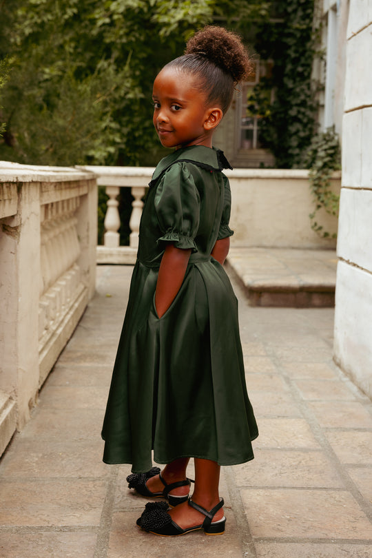 Young girl in a green dress standing on a stone pathway with greenery in the background