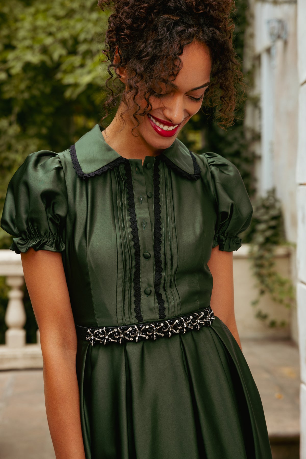 Woman wearing a green dress with a decorative belt, standing outdoors.