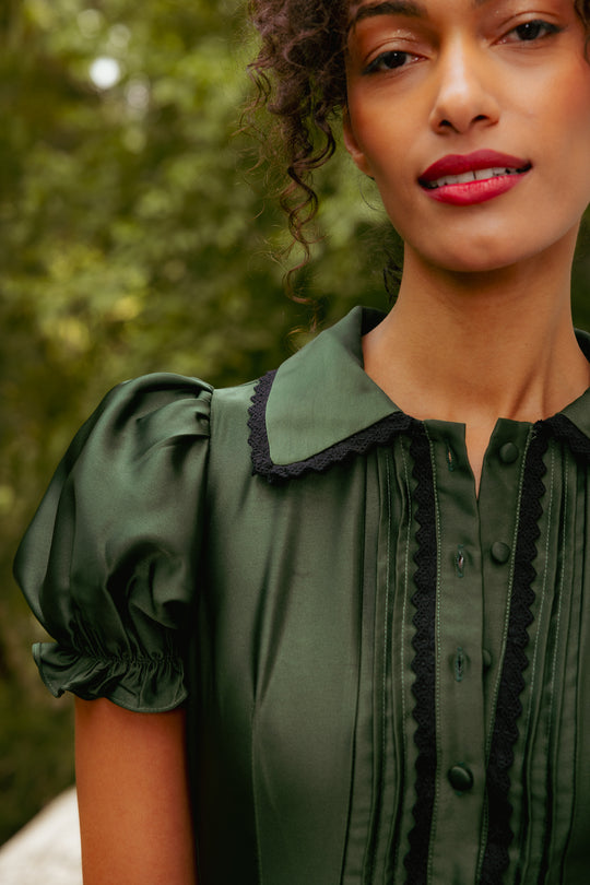 Woman wearing a green blouse with black trim against a blurred natural background