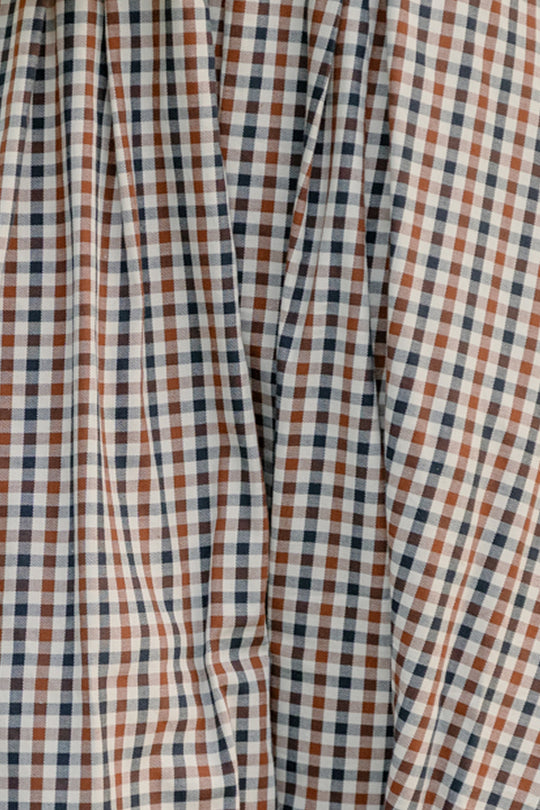 Close-up of fabric with a small chestnut gingham pattern in brown, navy blue, and white—perfect for a classic cotton skirt. The material showcases visible folds and creases, giving the Sophia Skirt in Chestnut Gingham by Ivy City Co a slightly wrinkled look that enhances its casual charm.