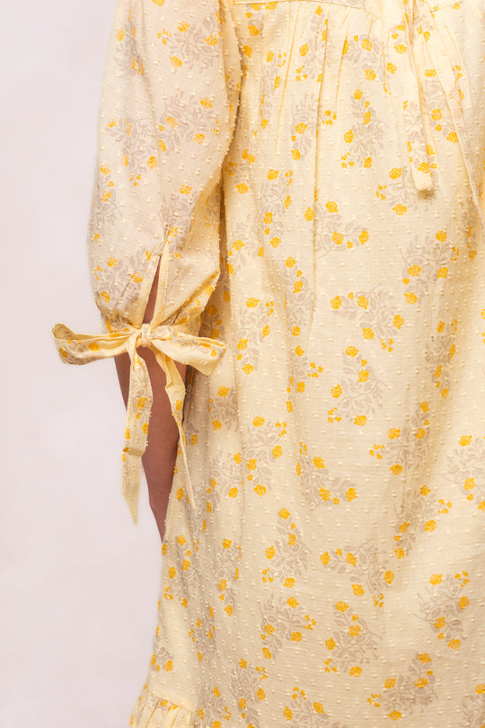 The Sunny Dress in Yellow Floral by Ivy City Co features a small floral print, tie detail on the below-elbow sleeve, and is made from textured swiss dot cotton.