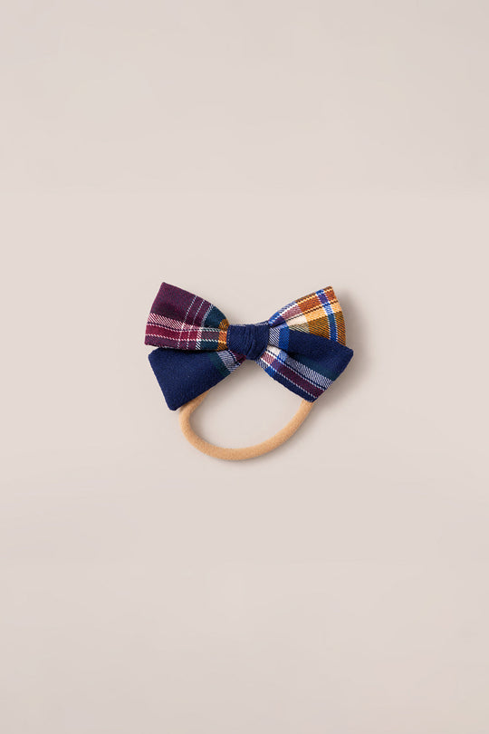 The Hair Bows in Midnight Plaid by Ivy City Co feature shades of navy, burgundy, and mustard plaid fabric attached to a beige elastic hairband, showcased on a simple light backdrop—a timeless Ivy City Co accessory.