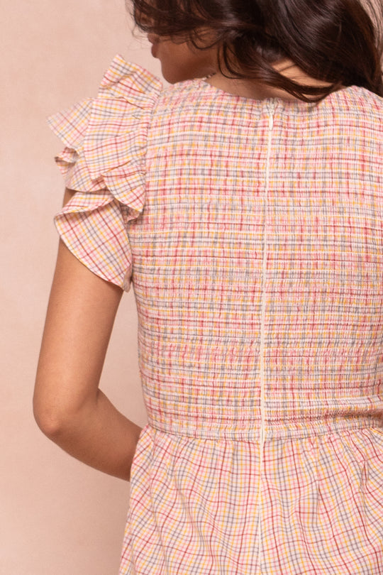 A woman is shown from the back wearing the Ivy City Co Hattie Jumpsuit in pastel multicolor gingham, featuring short ruffled sleeves, textured fabric, and a visible back zipper.