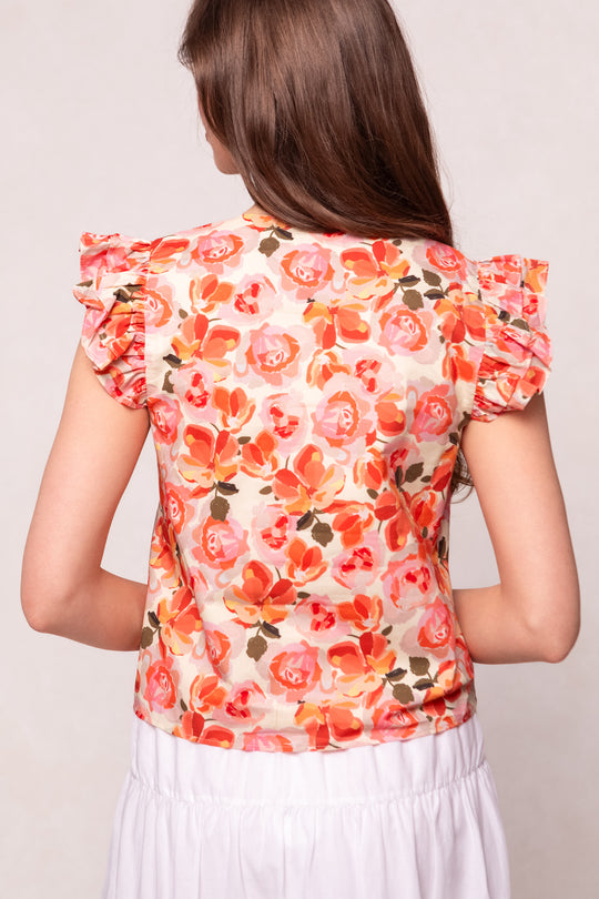 A woman with long brown hair, seen from behind, wears the Ivy City Co Lana Blouse in Pink Floral—a short-sleeved top with ruffled details—paired with a white skirt.