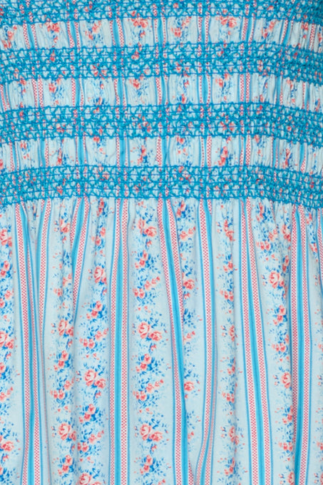 Close-up of the Sunday Best Dress in Rosette Linear Stripe by Ivy City Co: a light blue, maternity-friendly midi with pink and blue floral vertical stripes, blue thread smocking, and gathered detailing at the top.