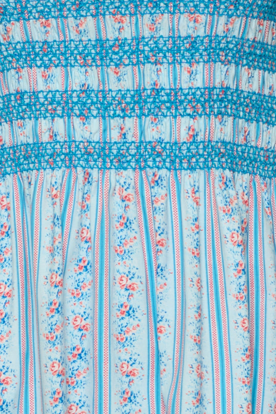 Close-up of the Sunday Best Dress in Rosette Linear Stripe by Ivy City Co: a light blue, maternity-friendly midi with pink and blue floral vertical stripes, blue thread smocking, and gathered detailing at the top.