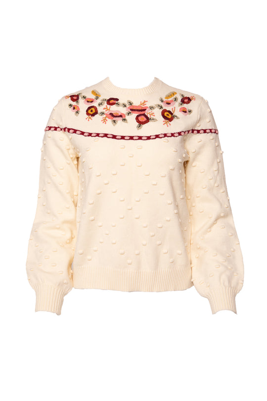 The Sylvie Sweater in Cream by Ivy City Co features textured polka dots, colorful floral embroidery, red ribbon accents, and a charming floral yoke. This maternity-friendly style blends comfort with eye-catching detail.