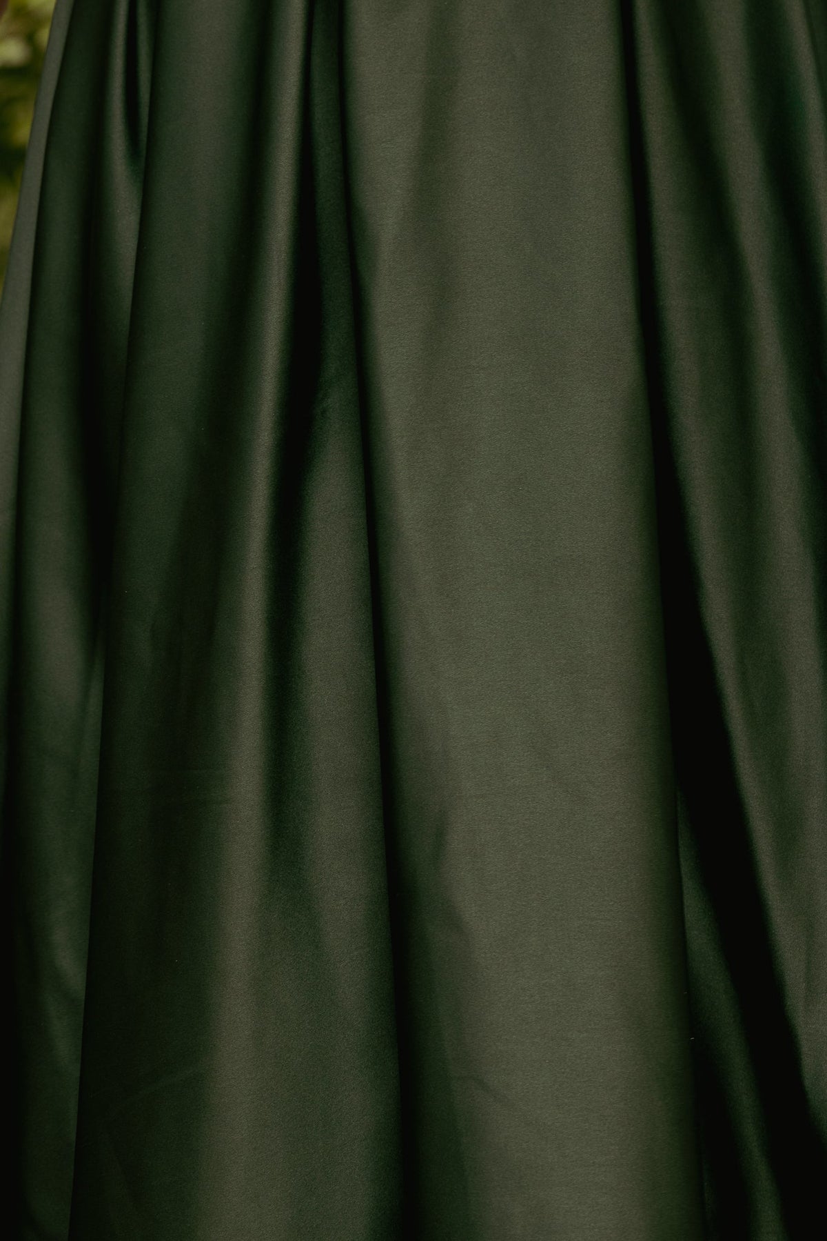 Close-up of the deep green satin fabric of the Sophia Dress in Green Satin, featuring soft vertical pleats.