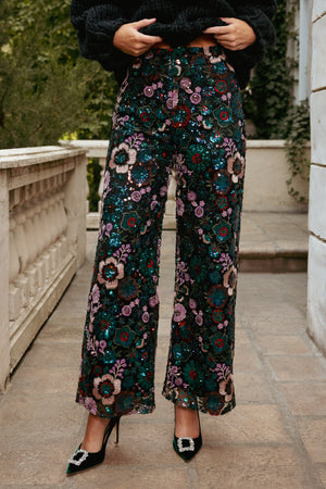 Person wearing floral sequin pants standing on a stone pathway.