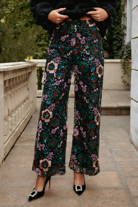 Person wearing floral sequin pants standing on a stone pathway.