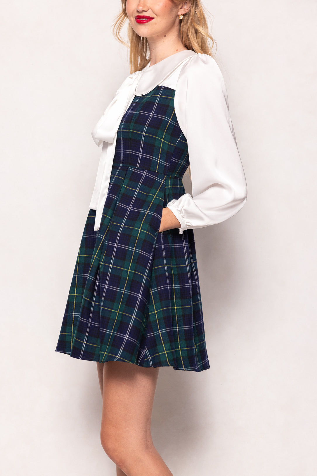 Woman wearing a plaid dress over a white blouse on a plain background