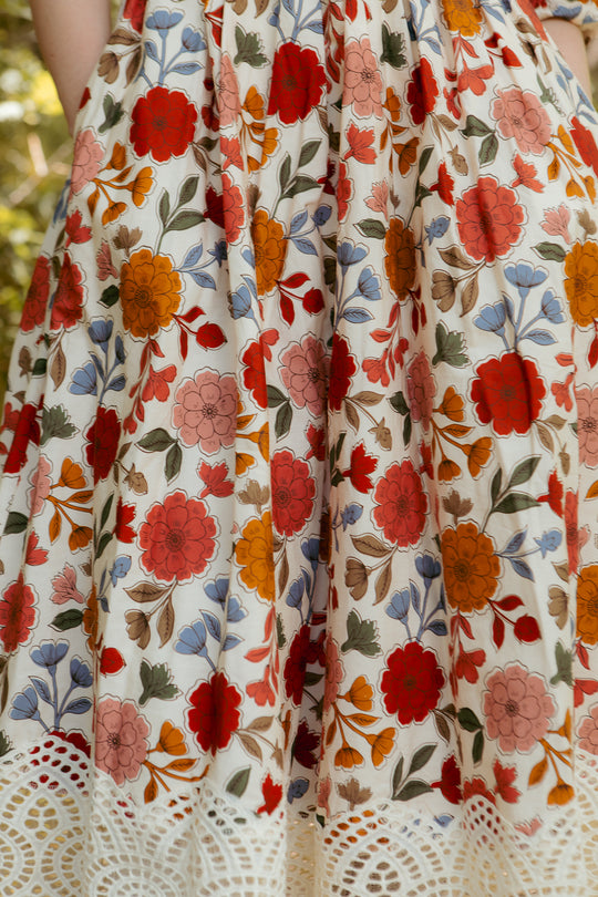 A close-up of Ivy City Cos Teagan Dress in Sepia Flower, a floral midi with vibrant red, orange, pink, and blue hues plus white lace hem trim—stylish and maternity friendly.