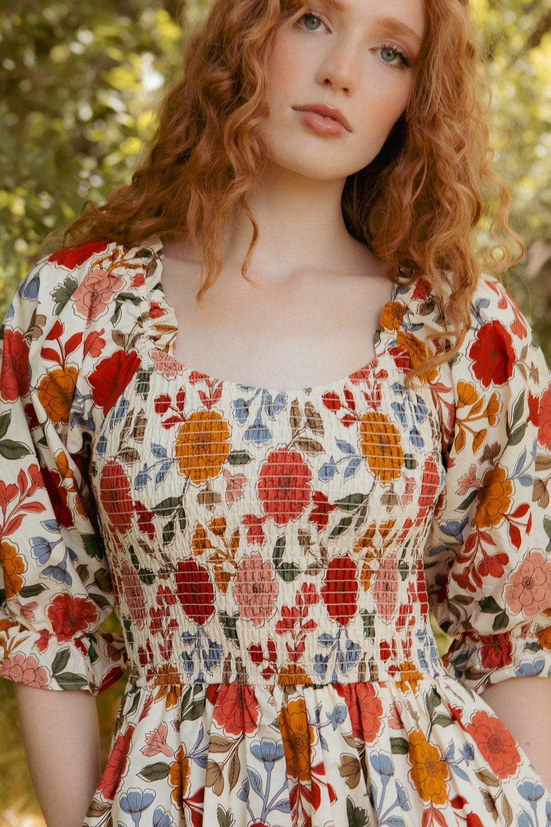 A red-haired woman wears the Teagan Dress in Sepia Flower by Ivy City Co, a maternity-friendly floral midi dress.