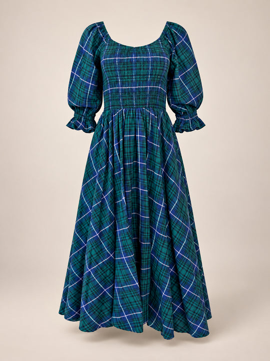 The Teagan Dress in Emerald Plaid by Ivy City Co is a long, green and blue plaid holiday dress featuring puffed sleeves, a fitted smocked bodice, and a flared skirt. With ruffled cuffs and a square neckline, this nursing-friendly dress is perfect for festive gatherings. Displayed against a neutral background.