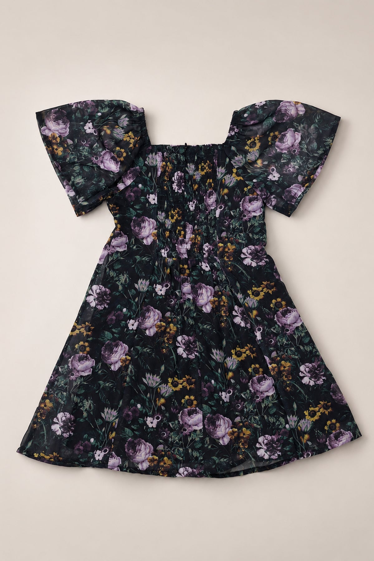 The Ivy City Co Teen Blakely Dress in Belladonna Bloom showcases a black background with a striking purple floral print, short off-shoulder flutter sleeves, a fitted ruched bodice, and a flared knee-length skirt—an ideal choice for those seeking a stylish girls’ dress.