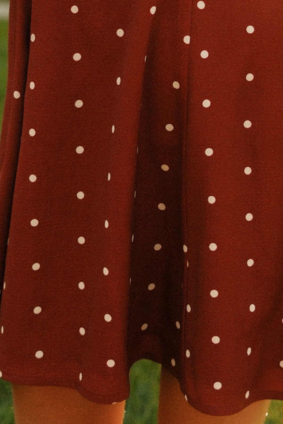 A close-up of the Ivy City Co Teen Blakely Dress in Cranberry Dainty Dot showcases its maroon fabric with white polka dots and reveals part of the wearer’s legs below the midi-length hem, capturing its playful style.