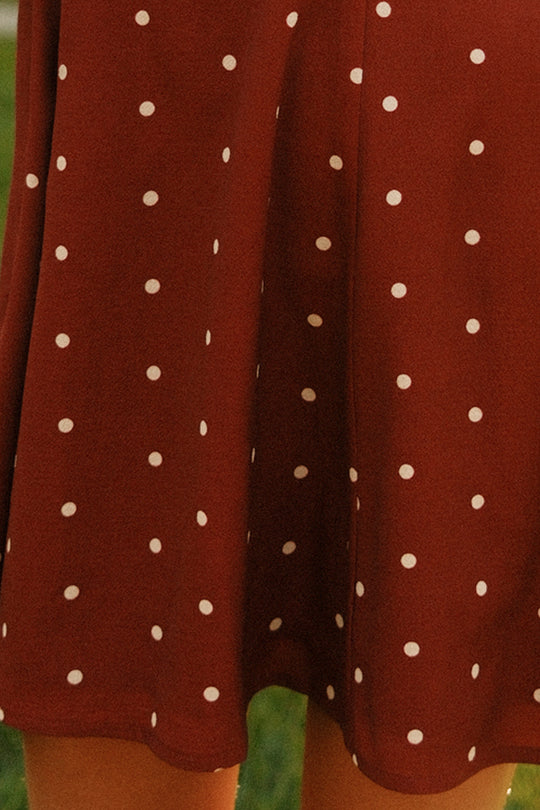 A close-up of the Ivy City Co Teen Blakely Dress in Cranberry Dainty Dot showcases its maroon fabric with white polka dots and reveals part of the wearer’s legs below the midi-length hem, capturing its playful style.