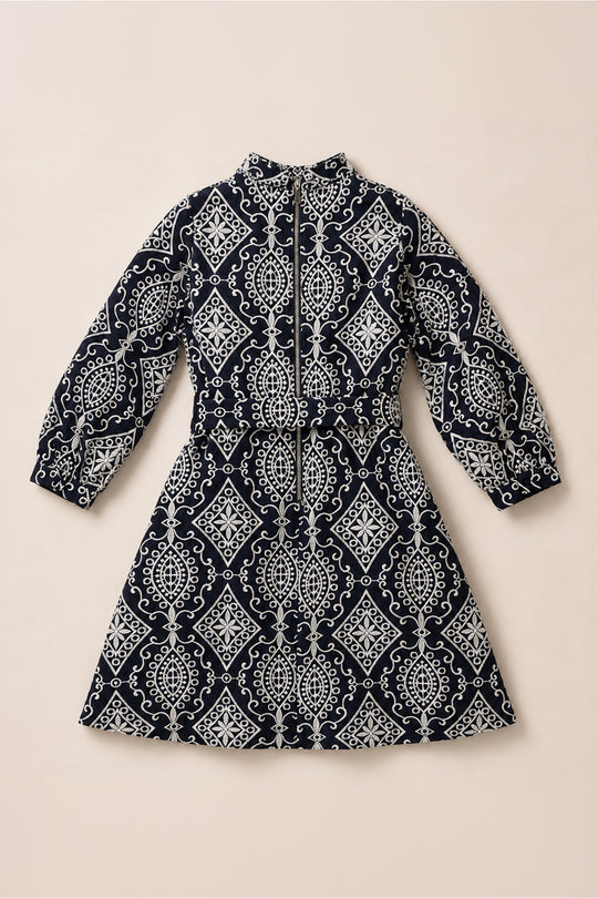 Navy blue long-sleeve Teen Clover Dress in Midnight Tile by Ivy City Co, featuring a white geometric and floral pattern, belted at the waist and displayed flat on a light beige background. This elegant midi-length dress effortlessly combines style and comfort.